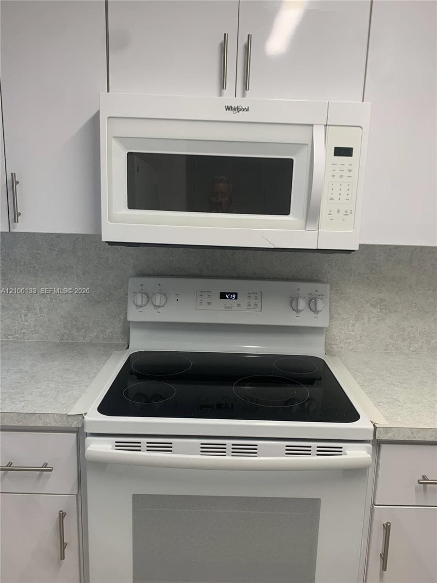 White cabinetry with brushed metal hardware, solid-surface countertops, over-the-range microwave, and electric smooth-top range
