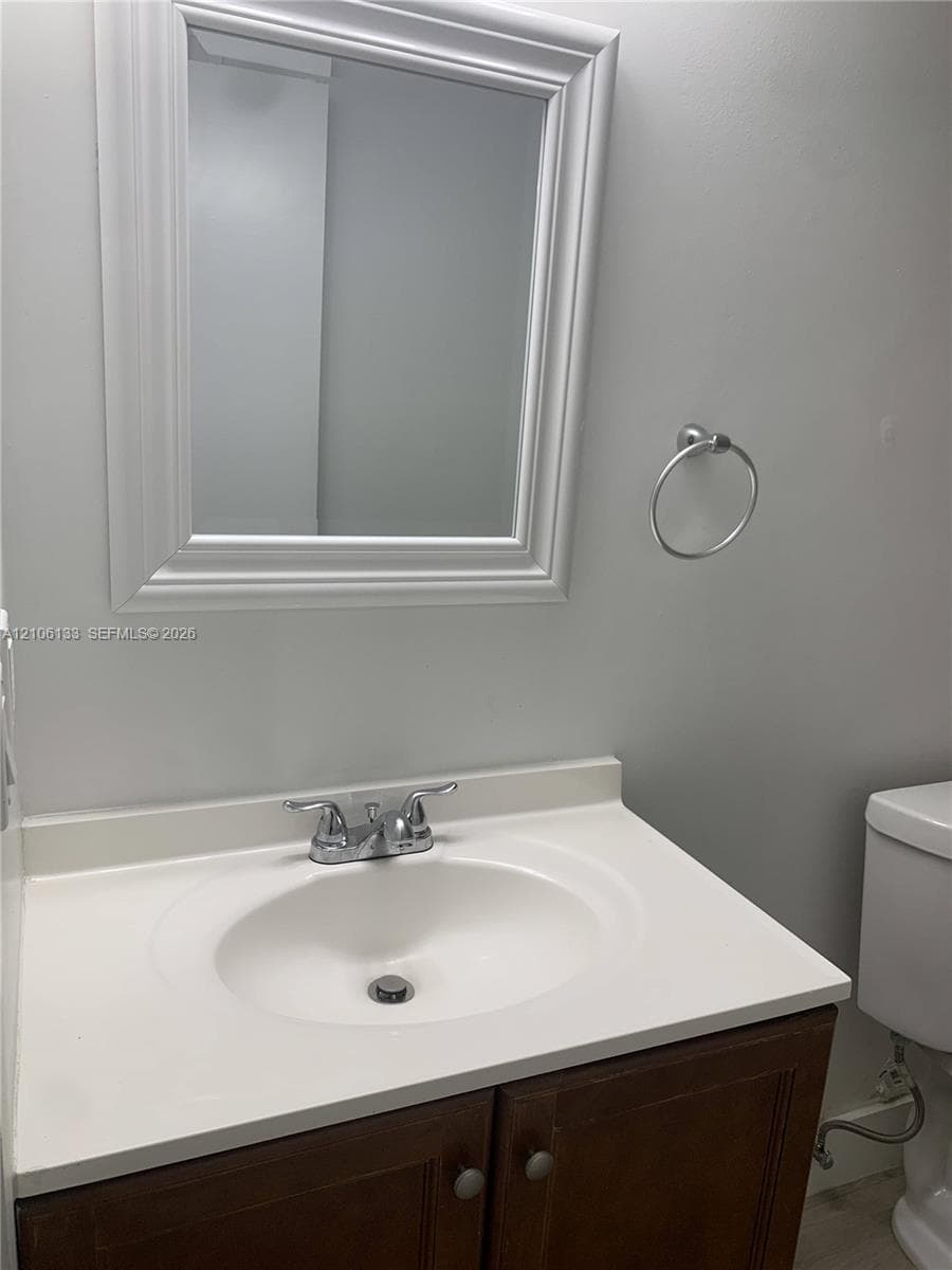 Vanity featuring a dark-finish wood cabinet, solid-surface countertop with an integrated basin, chrome-finish double-handle faucet, framed wall-mounted mirror, and wall-mounted ring towel holder