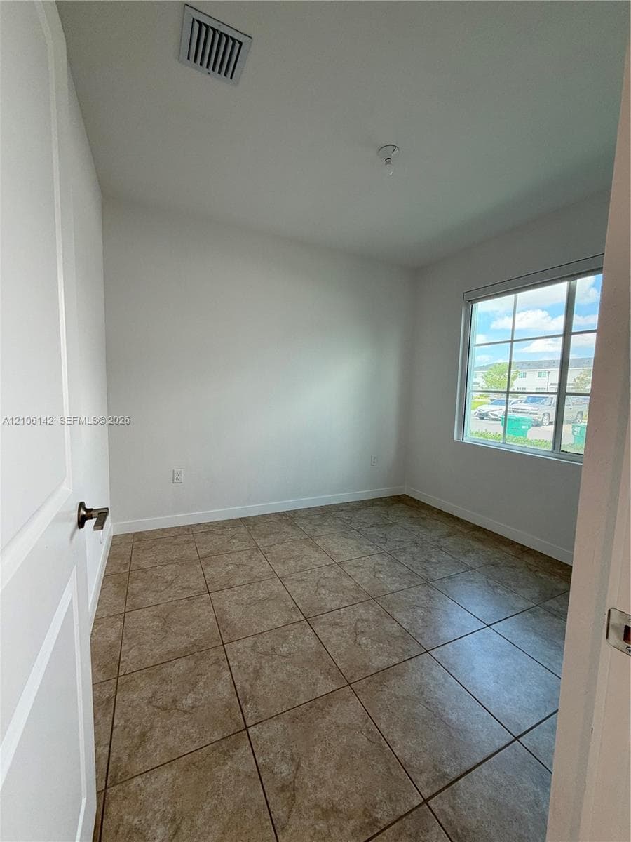 Neutral-toned interior space featuring large-format ceramic tile flooring, a multi-pane window with natural light, and a white paneled interior door