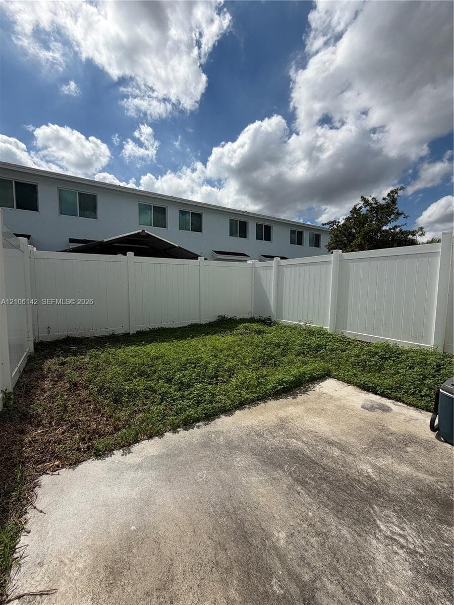 Private backyard area featuring a concrete patio, grassy lawn, and tall white vinyl privacy fencing