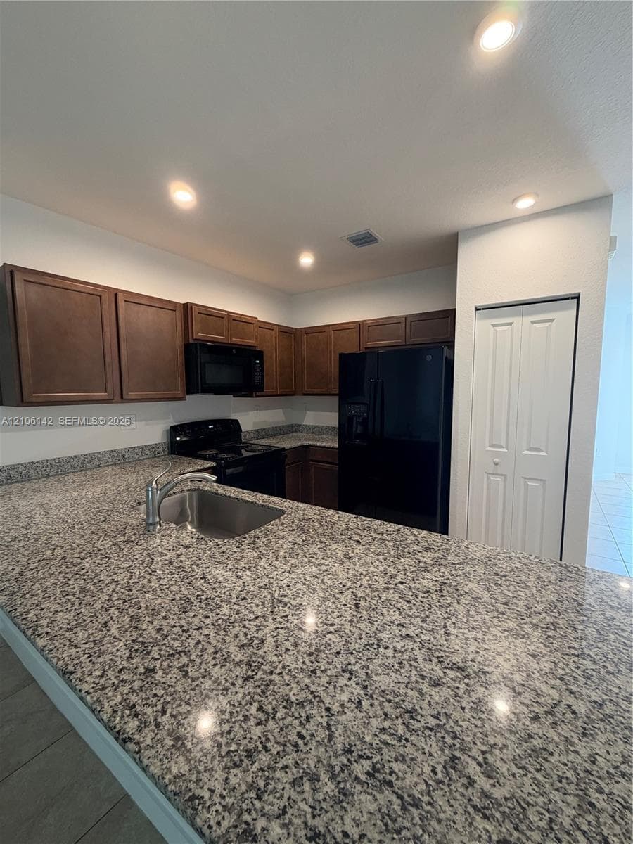 Kitchen featuring stone countertops, dark wood cabinetry, recessed lighting, integrated black appliances, and an undermount stainless steel sink