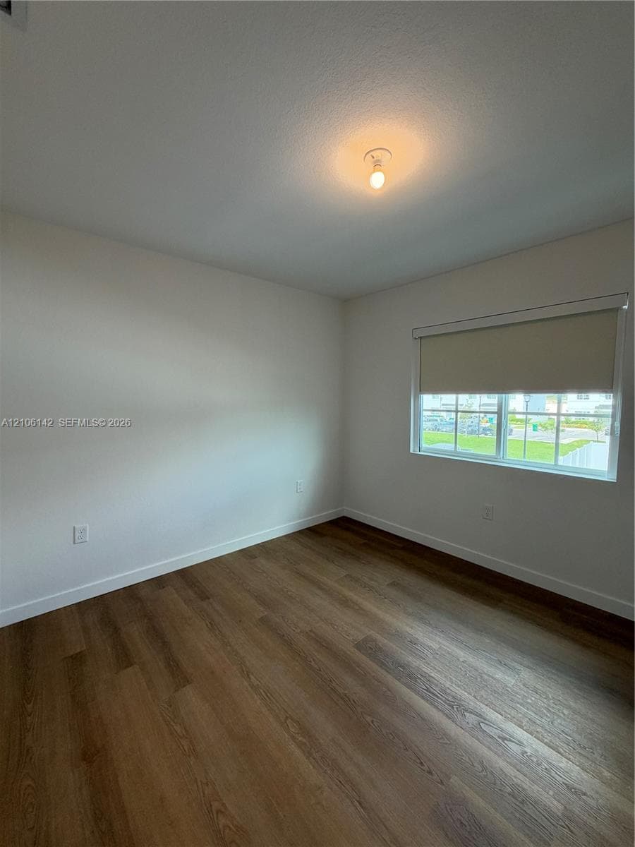 Room featuring wood-finish flooring, neutral walls, a single-pane window with a retractable shade, and a flush-mount ceiling light fixture