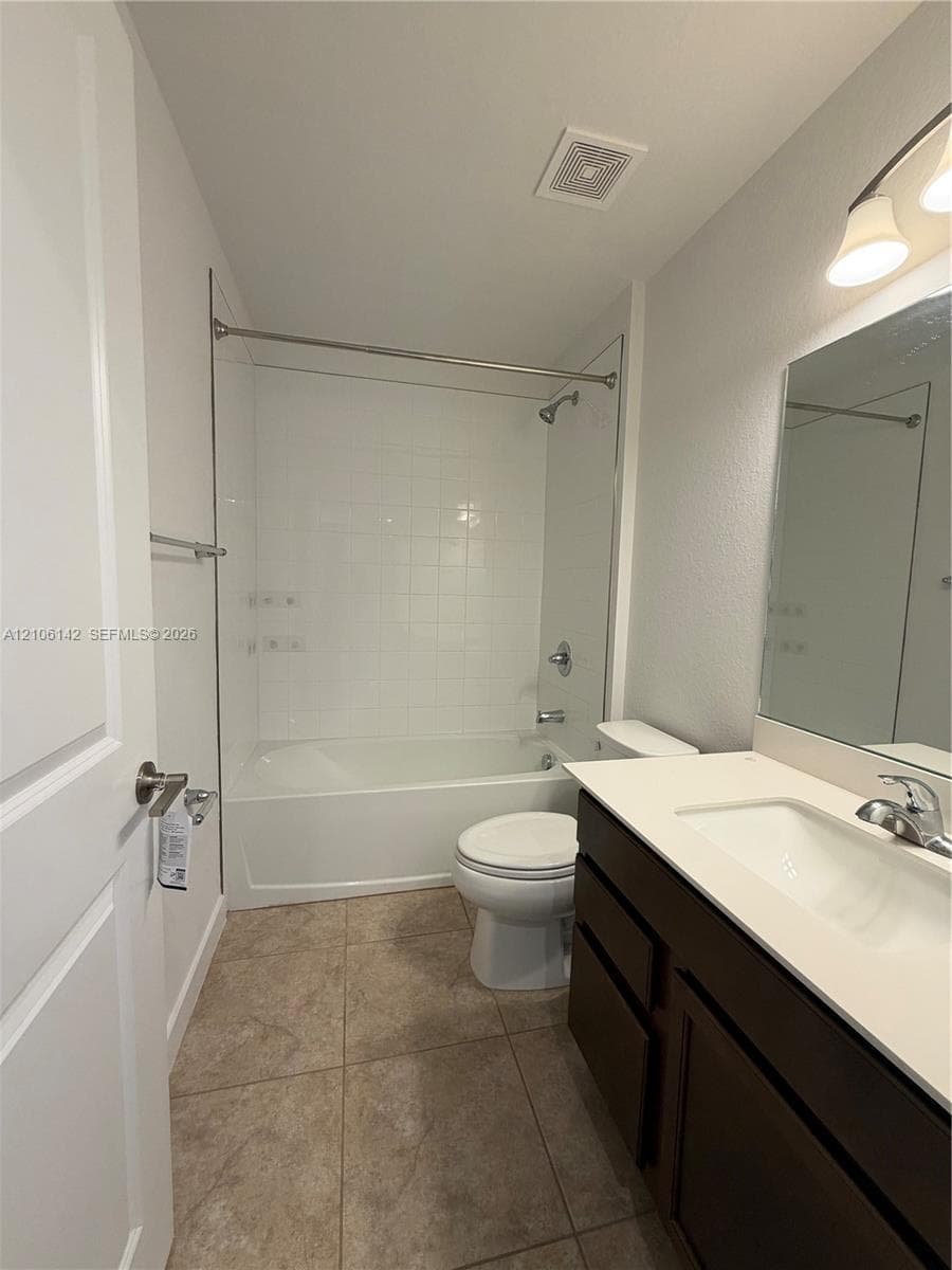 Bathroom featuring a dark-finish vanity with a light-tone countertop, an undermount sink, a tiled bathtub surround, and a wall-mounted mirror