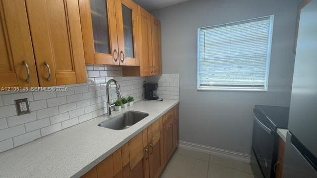 Kitchen featuring natural finish shaker cabinetry, light-toned stone-composite countertops, subway tile backsplash, stainless steel undermount sink, and polished chrome pull-down faucet