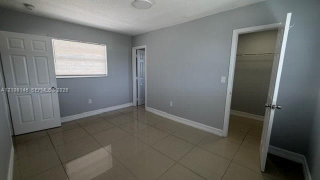 Room featuring large-format tile flooring, neutral wall tones, multi-panel interior doors, and a walk-in closet with built-in shelving