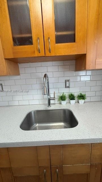 Undermount stainless steel sink featuring a chrome pull-down faucet, quartz countertop, white subway tile backsplash, and wood cabinetry with glass-panel inserts