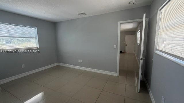 Interior room featuring large-format tile flooring, neutral wall paint, and dual windows with horizontal blinds