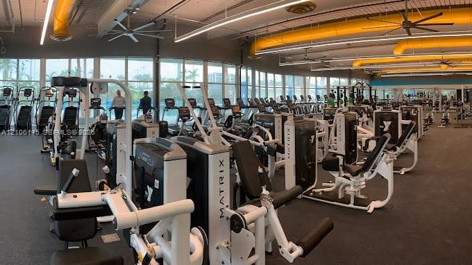 Fitness center featuring floor-to-ceiling windows, industrial-style exposed ductwork, rubberized flooring, and high-clearance ceiling fans