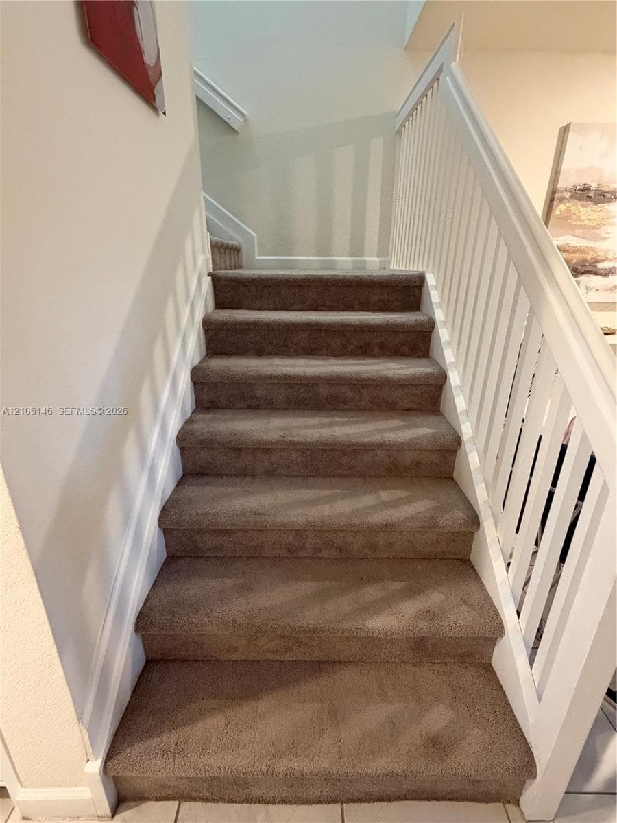 Staircase featuring wall-to-wall carpeting, white wooden balusters, and a painted handrail