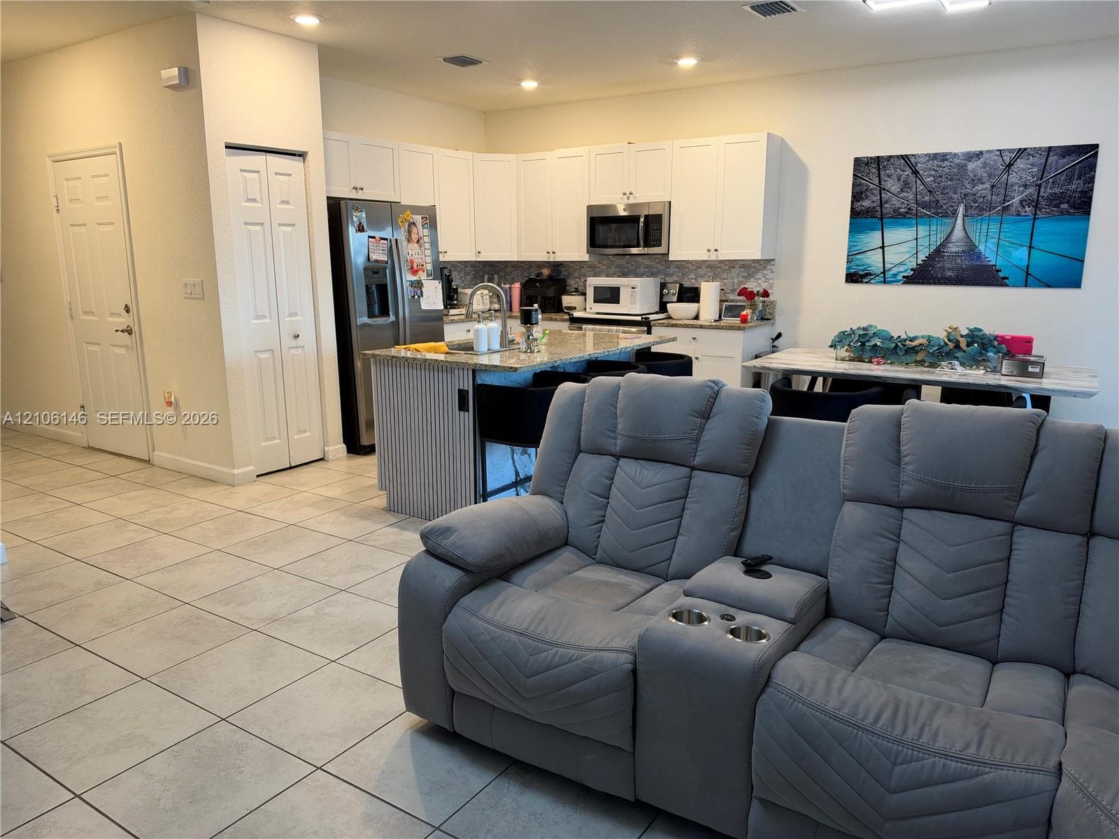 Kitchen featuring white shaker-style cabinetry, stone-finish countertops, a central island with a fluted detail finish, stainless steel appliances, and large-format ceramic tile flooring