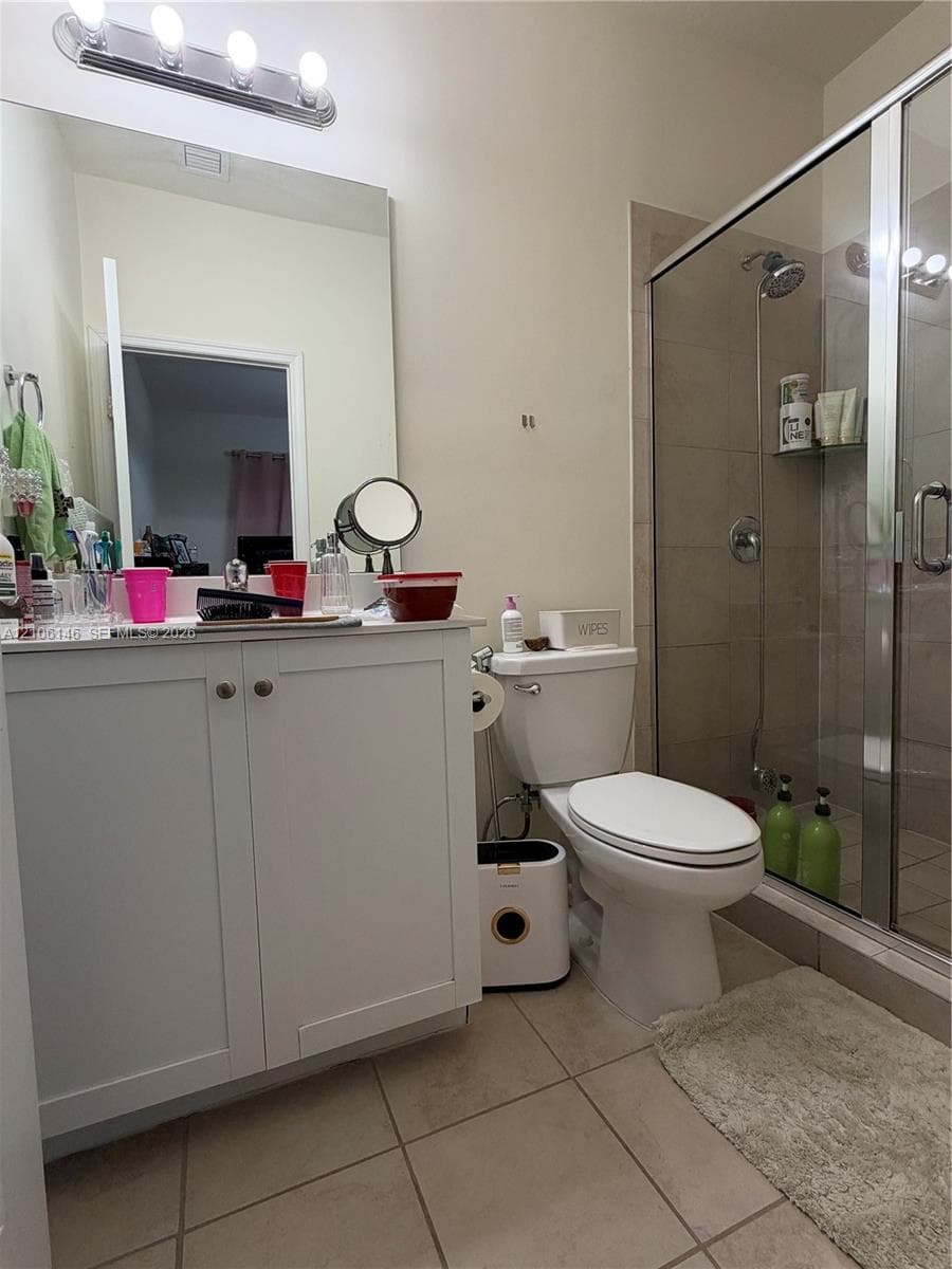 White vanity cabinet with a countertop, large vanity mirror, four-light vanity fixture, and a tiled shower enclosure with a glass door