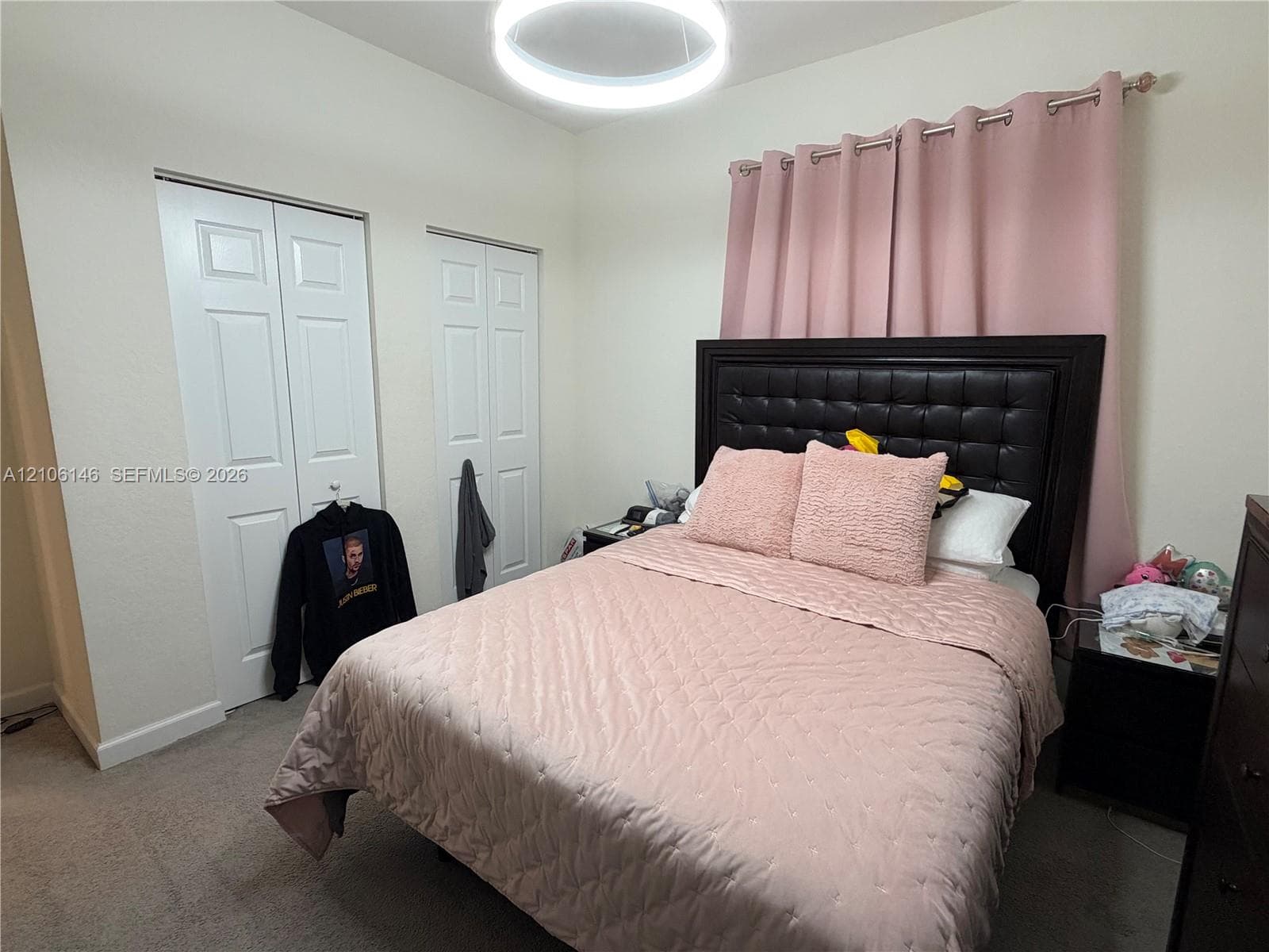 Neutral wall color, wall-to-wall carpeting, dual white panel doors for closet storage, and a modern circular LED flush-mount ceiling fixture