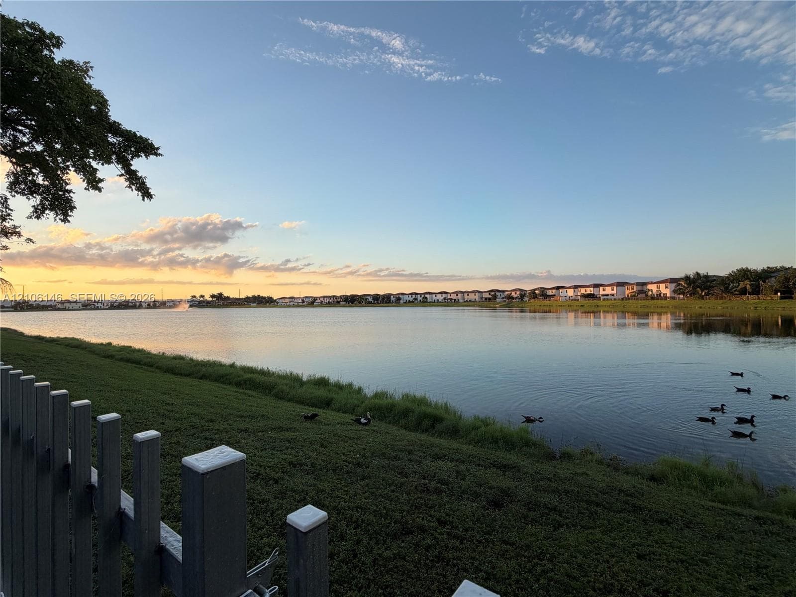 Waterfront property featuring a lake, sloped grass embankment, and vinyl post-and-rail fencing