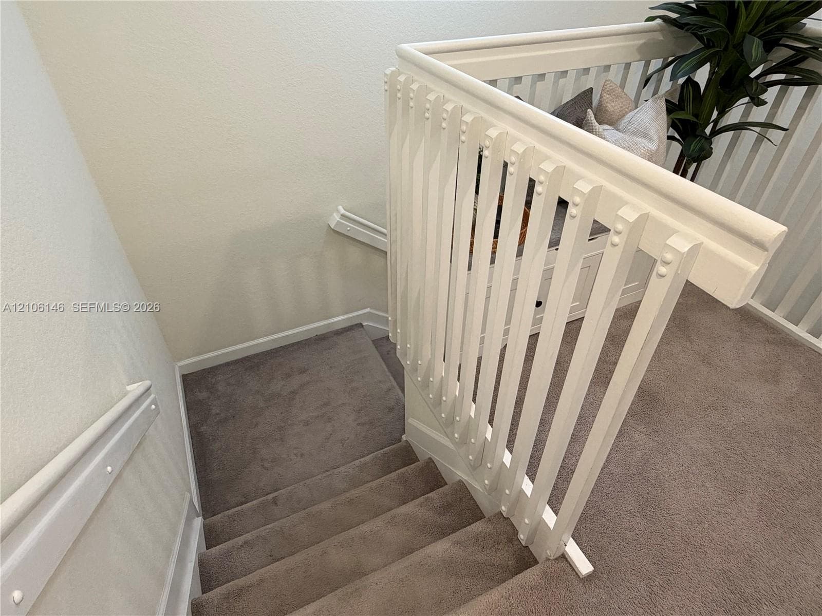 Staircase featuring neutral-toned carpeting, white painted wooden balusters, a matching handrail, and built-in storage cabinetry