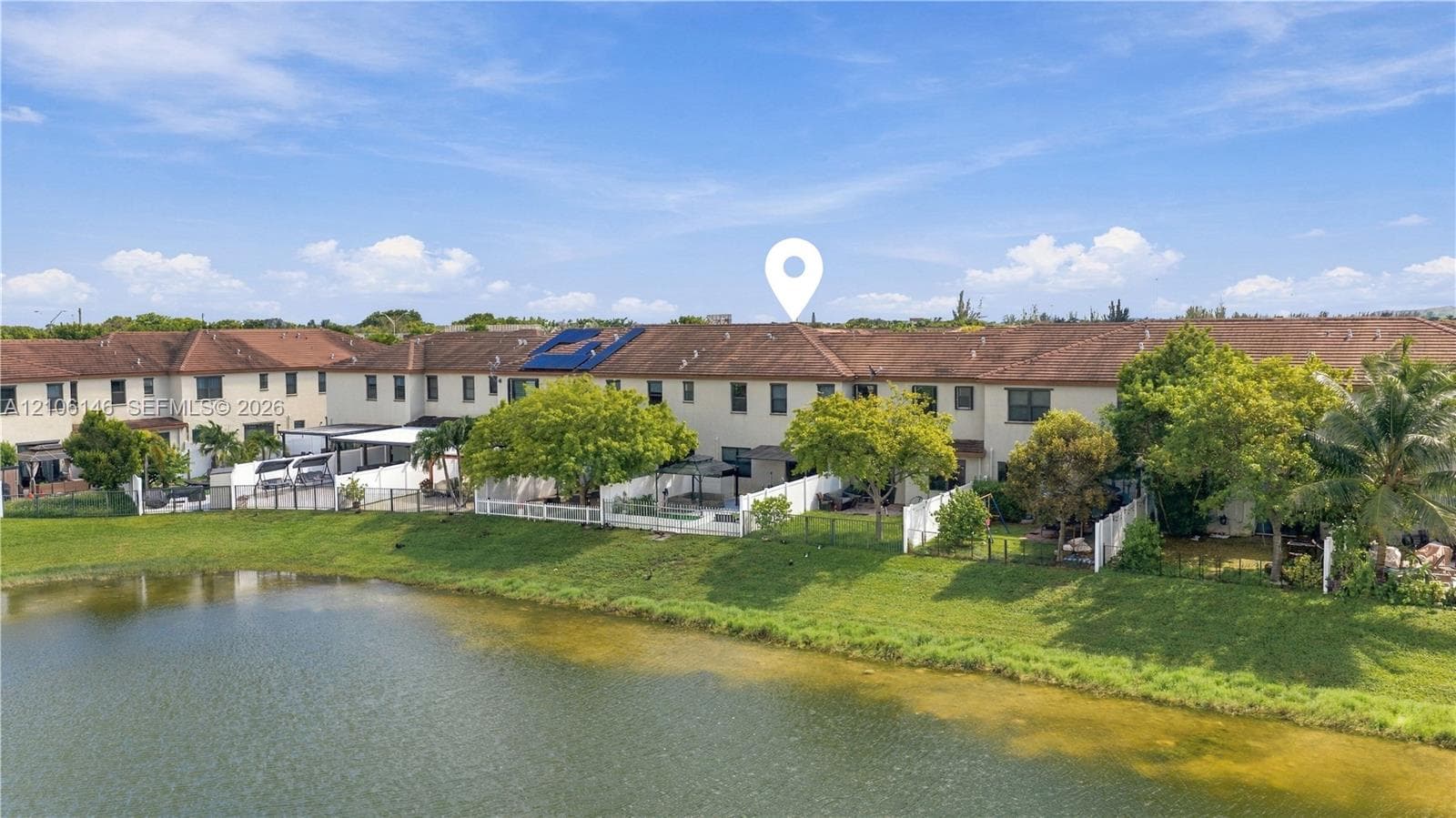 Stucco exterior townhouse featuring a tile roof, solar panels, and a private enclosed rear patio situated on a pond