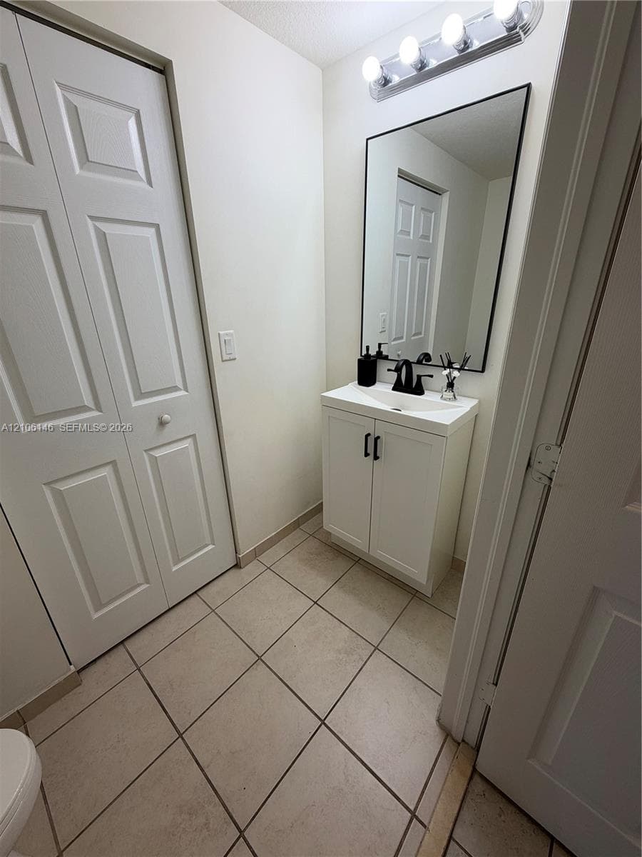White vanity with a rectangular sink, matte black faucet, framed mirror, and tiled flooring