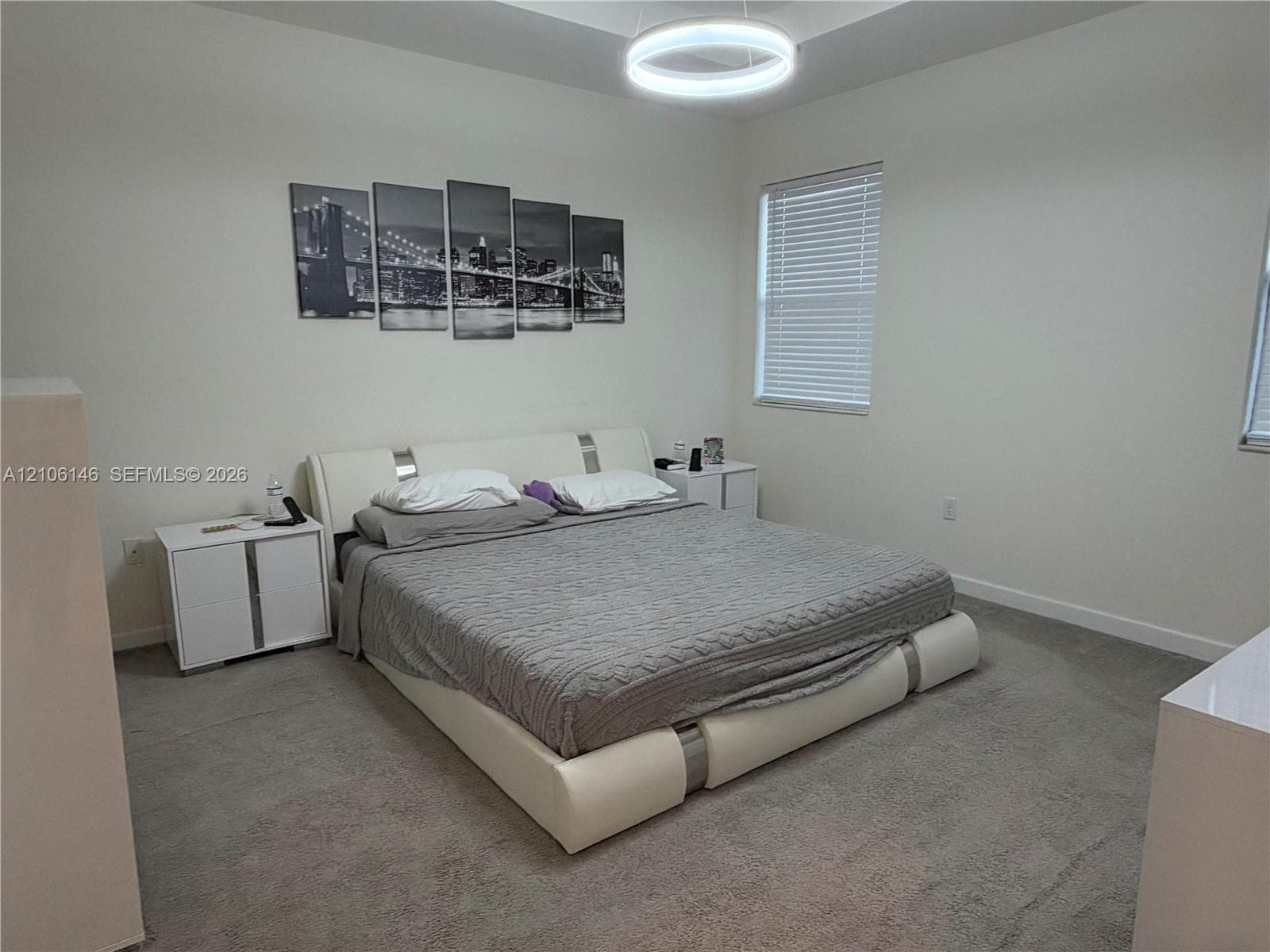 Tray ceiling featuring a contemporary circular LED light fixture, carpeted flooring, and windows with horizontal blinds