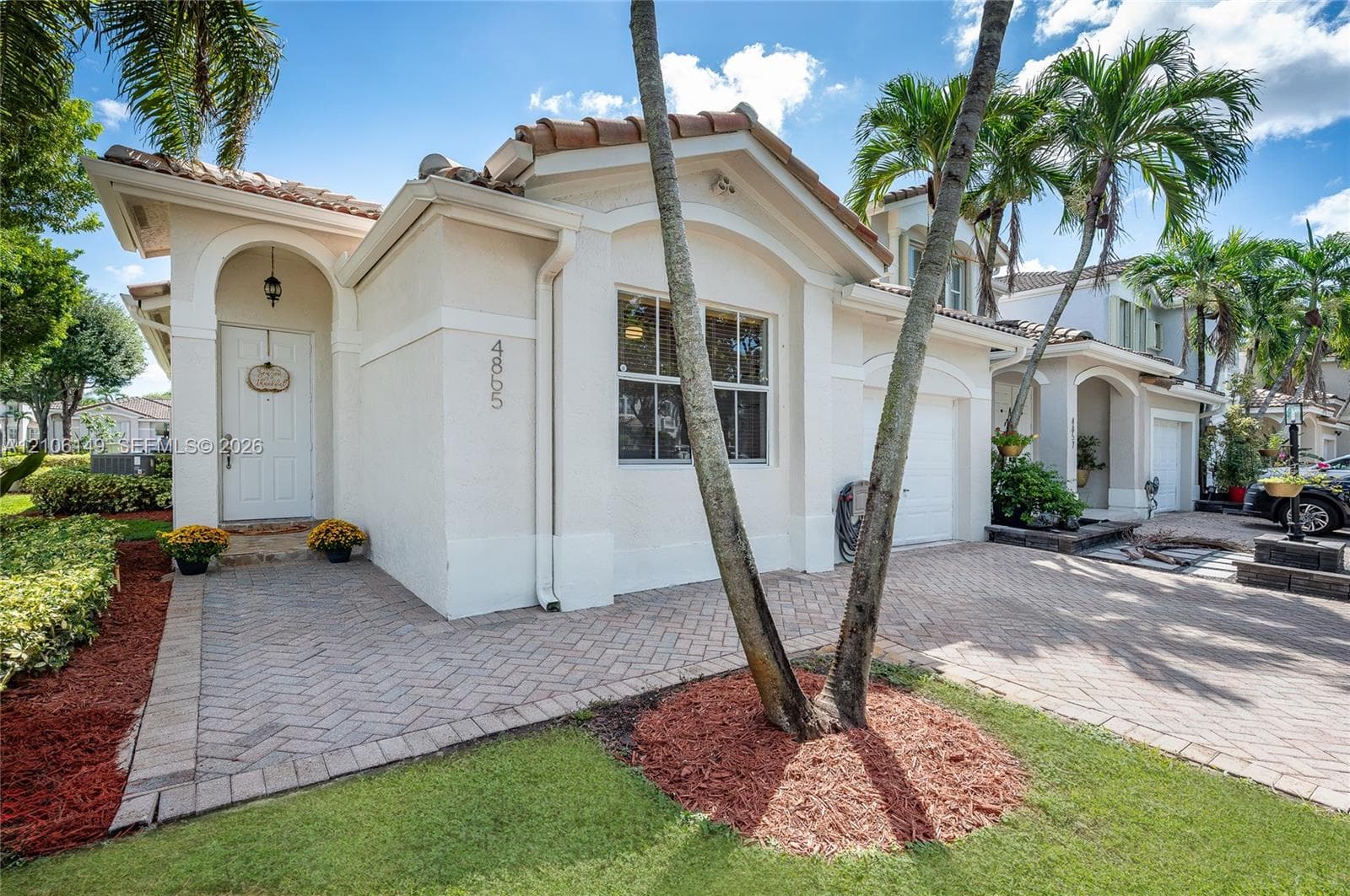 Stucco exterior with a tiled roof, arched entryway, brick-paver driveway, and single-car garage