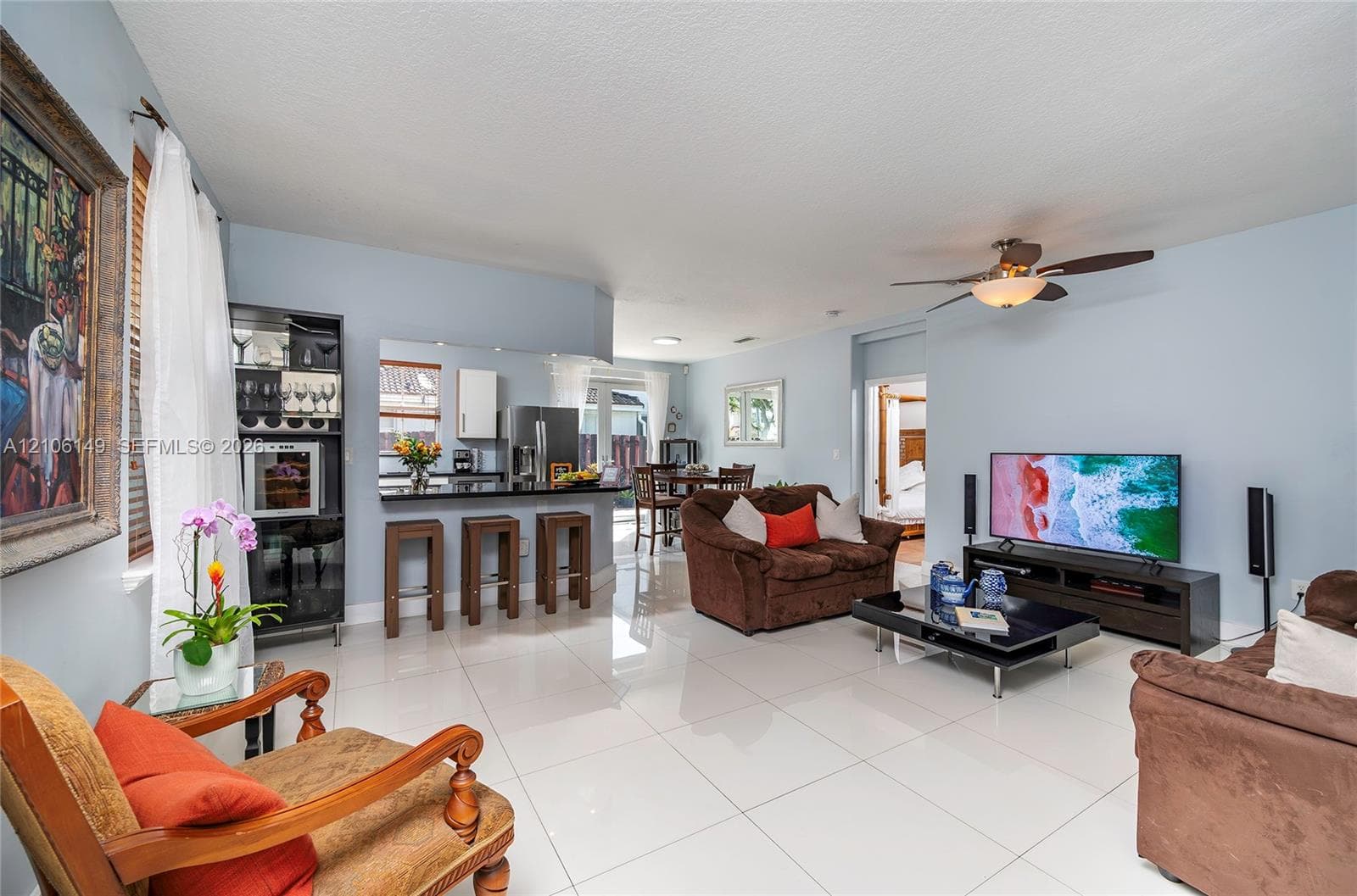 Open-concept living space featuring high-gloss tile flooring, kitchen breakfast bar, built-in cabinetry, and ceiling fan with integrated lighting