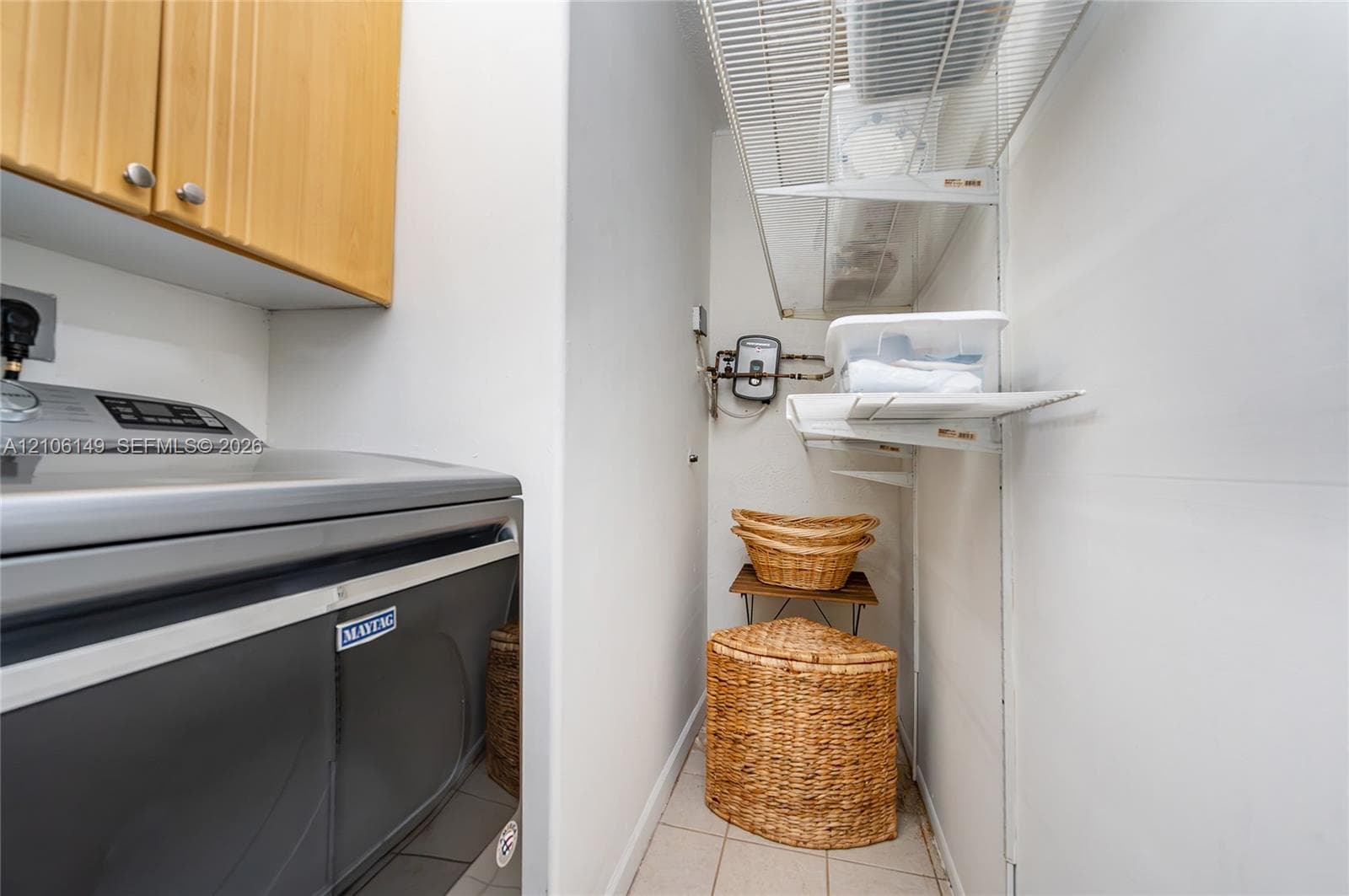 Utility area featuring wall-mounted upper cabinetry, tiled flooring, and tiered wire shelving
