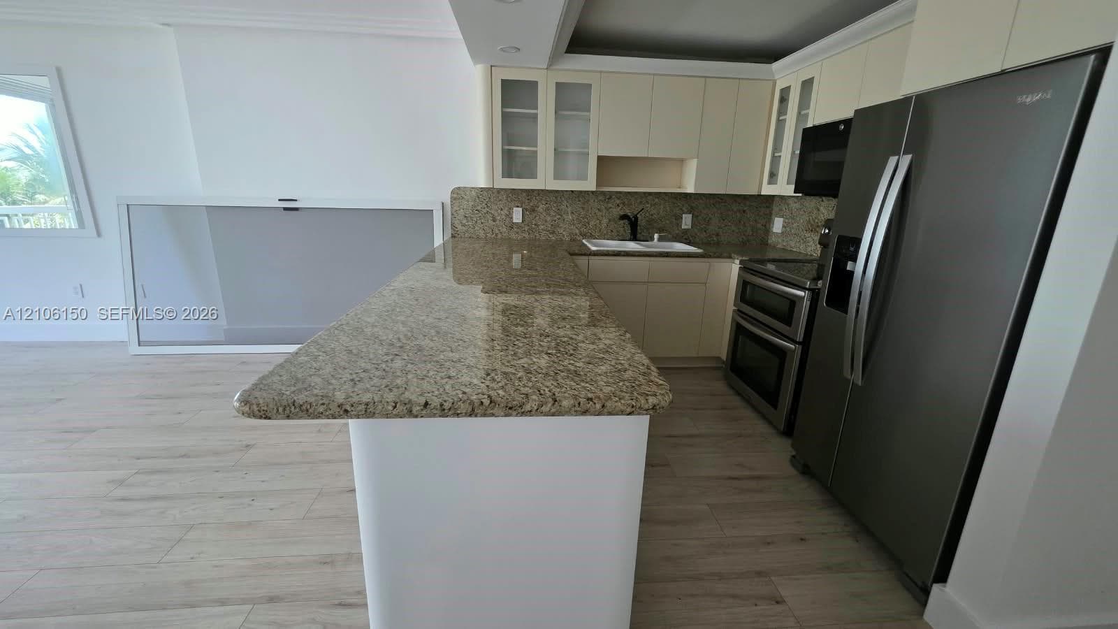 Kitchen featuring an expansive stone countertop, stainless steel appliances, light-toned cabinetry, and wood-finish flooring