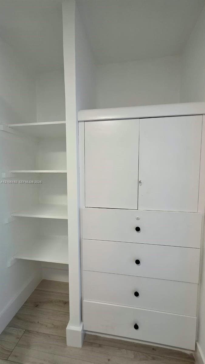 Built-in storage cabinet featuring four drawers and dual upper doors, accompanied by integrated open shelving and wood-finish flooring