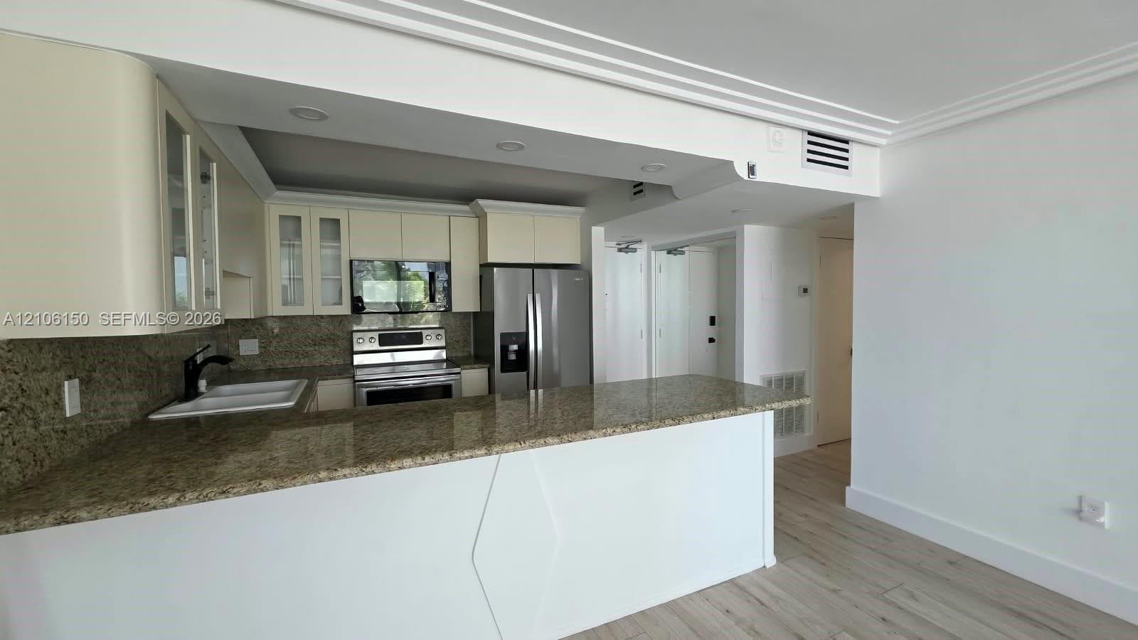 Kitchen featuring stone countertops, breakfast bar, stainless steel appliances, upper cabinetry with glass-panel doors, and wood-finish flooring