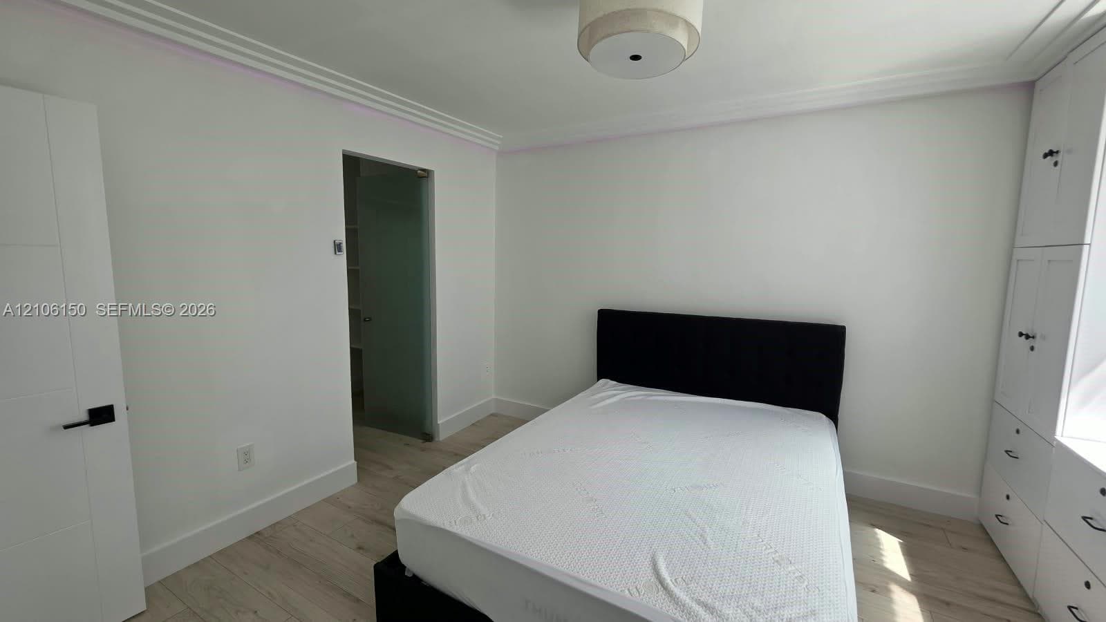 Room featuring wood-finish flooring, crown molding, built-in floor-to-ceiling cabinetry, a flush-mount drum ceiling light, and a door with matte black hardware