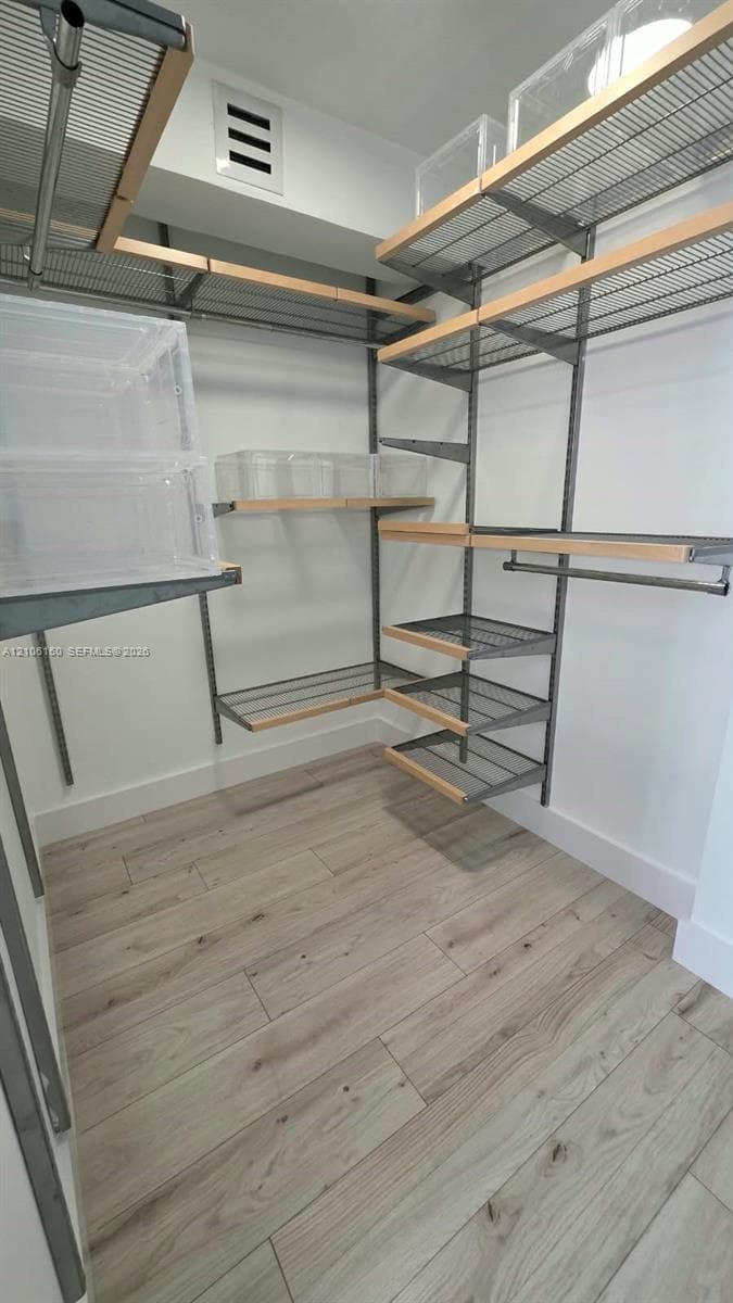Walk-in closet featuring adjustable metal wire shelving, wood-trim edging, and wood-finish flooring