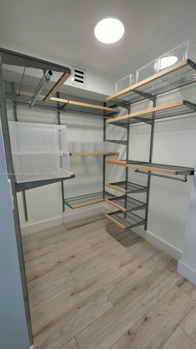 Storage space featuring adjustable metal wire shelving, integrated wood-trim detailing, dual hanging rods, and wood-finish tile flooring