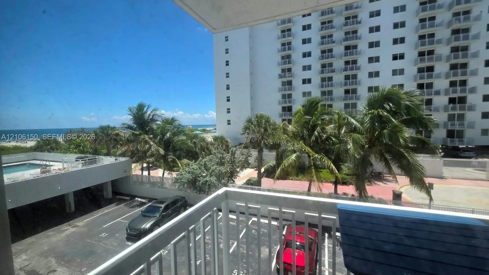 Private balcony featuring metal railings overlooking coastal grounds, palm trees, and an outdoor swimming pool