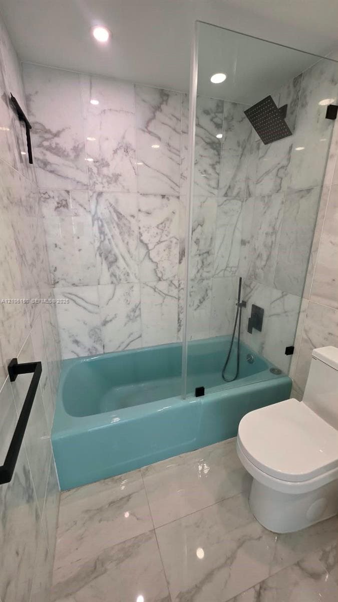 Full-height stone-finish wall tile, frameless glass shower panel, overhead rainfall showerhead, handheld shower fixture, and matte black hardware