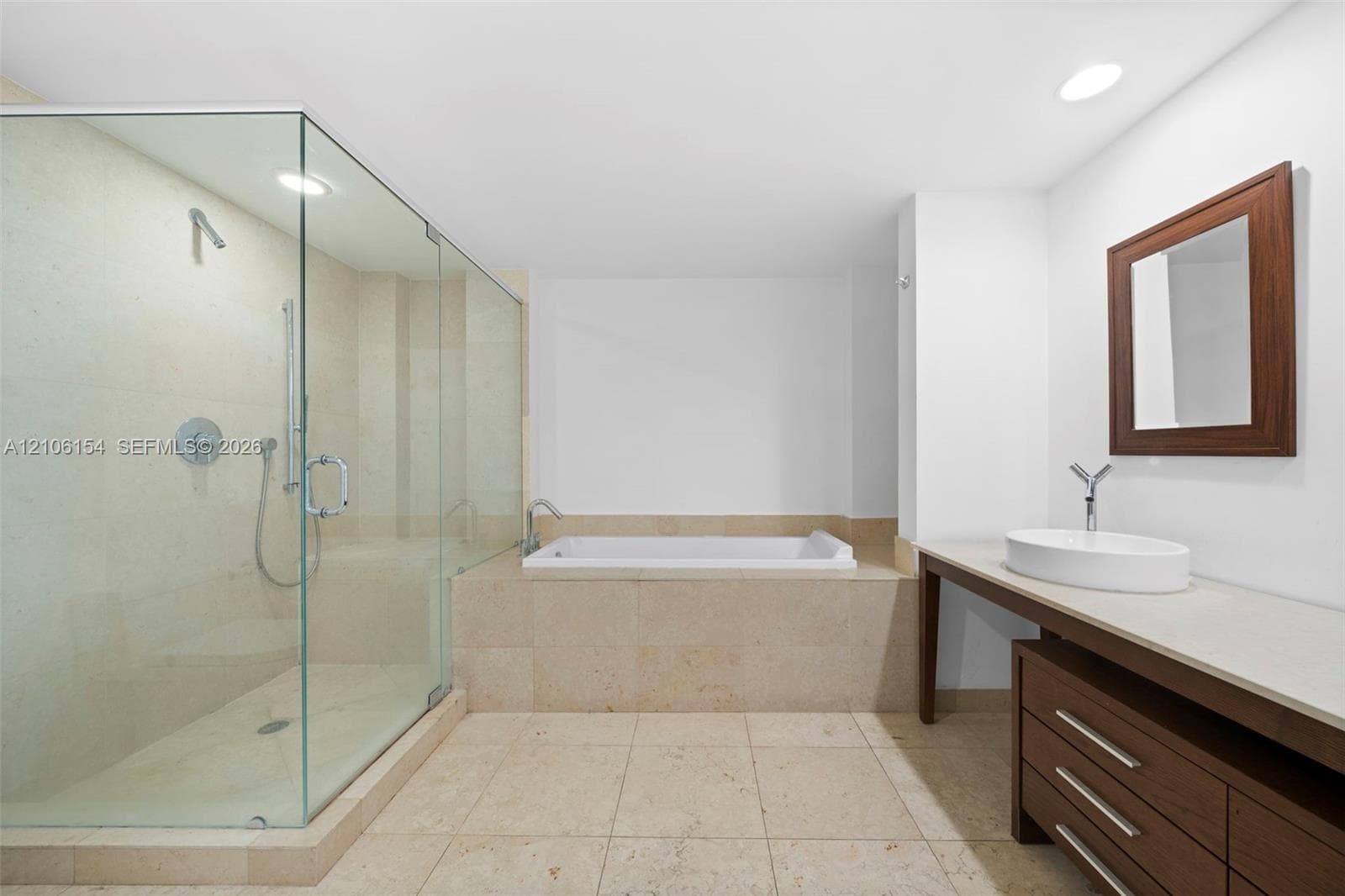 Bathroom featuring a glass-enclosed walk-in shower, a tiled soaking tub, custom wood-finish cabinetry, a vessel sink, and stone-finish flooring