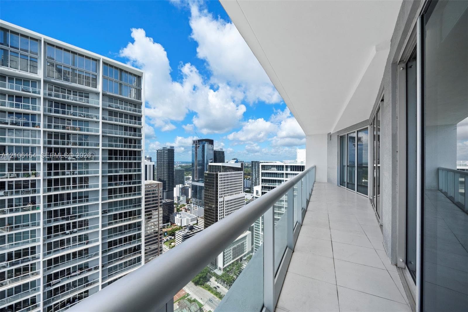 Private balcony featuring large-format tile flooring, glass panel railing, and metal handrail