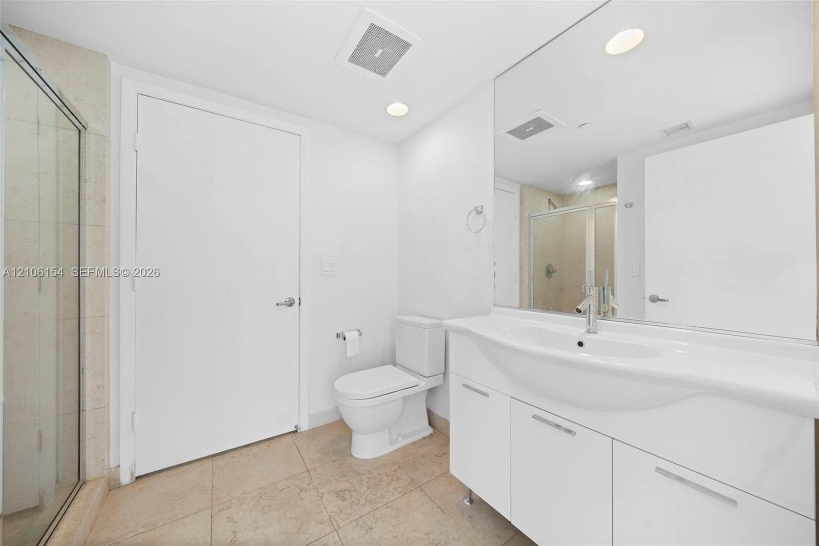 Full-width vanity with integrated sink, stone-finish tile flooring, glass-enclosed shower, expansive wall-mounted mirror, and recessed lighting