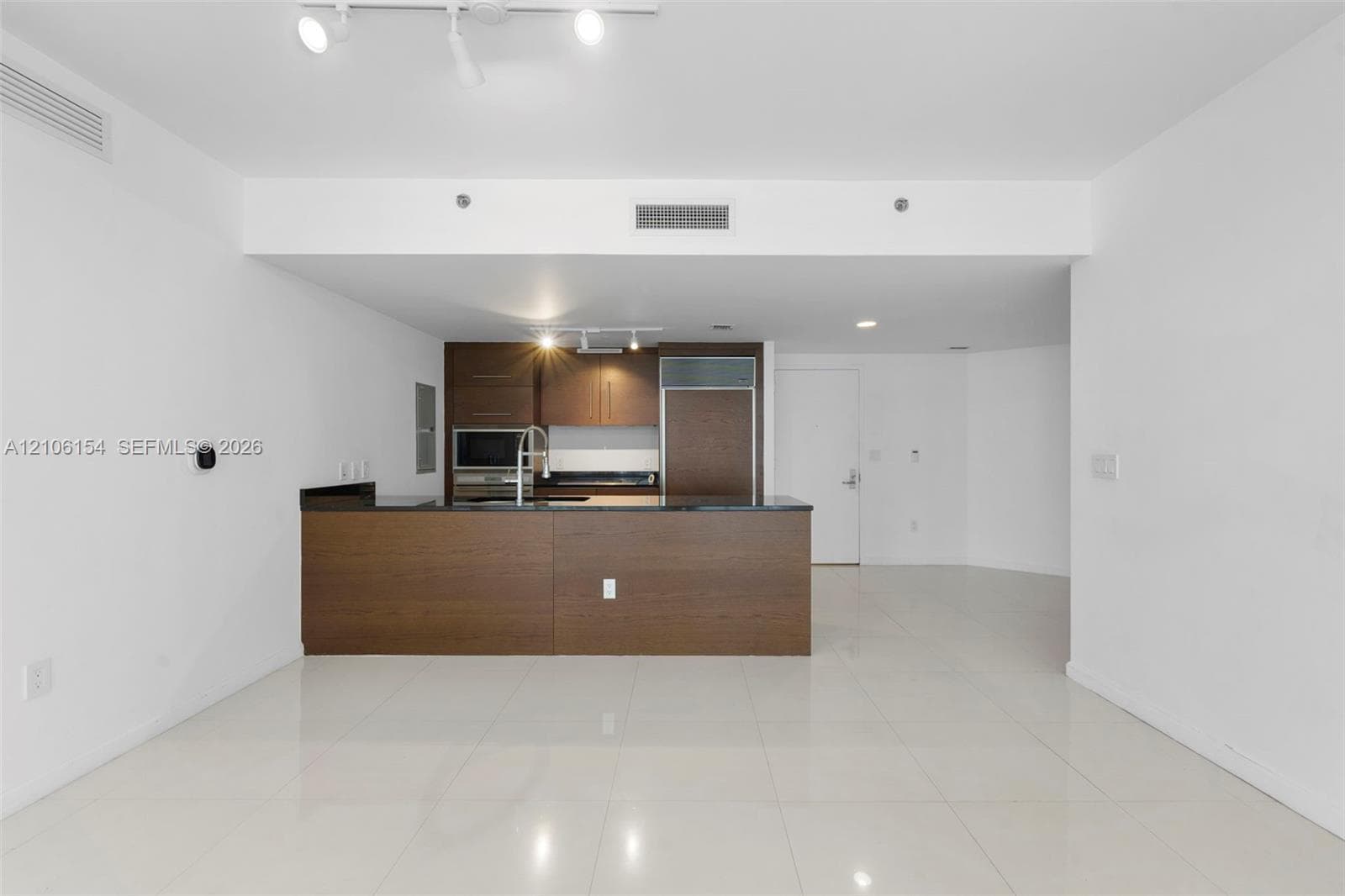 Kitchen featuring flat-panel wood-finish cabinetry, dark stone countertops, integrated refrigerator, stainless steel microwave, and tile flooring