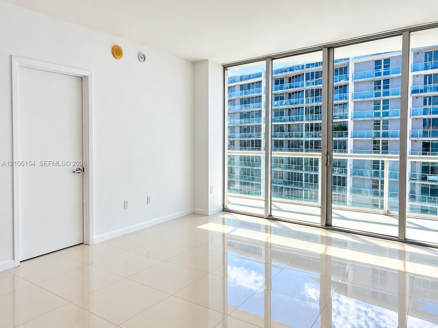 Floor-to-ceiling glass paneling, polished light-tone tile flooring, and a private balcony access point