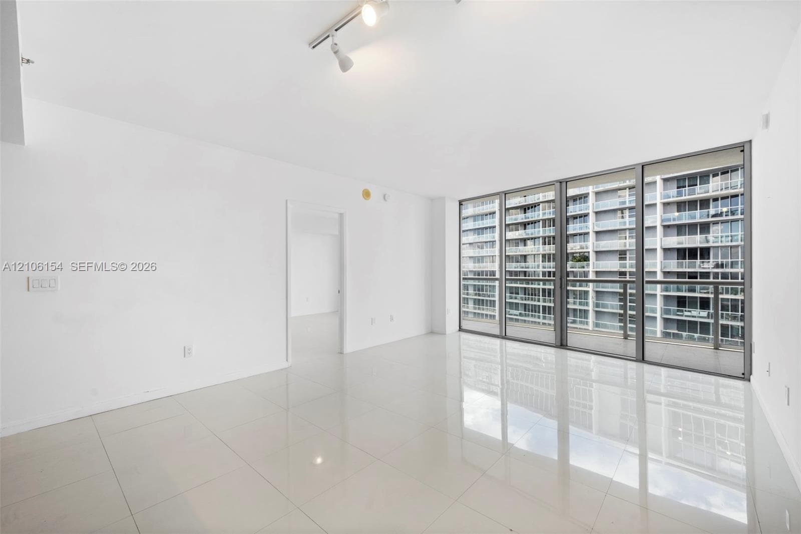 Open floor plan featuring polished light-tone tile flooring, floor-to-ceiling glass wall panels, and adjustable track lighting