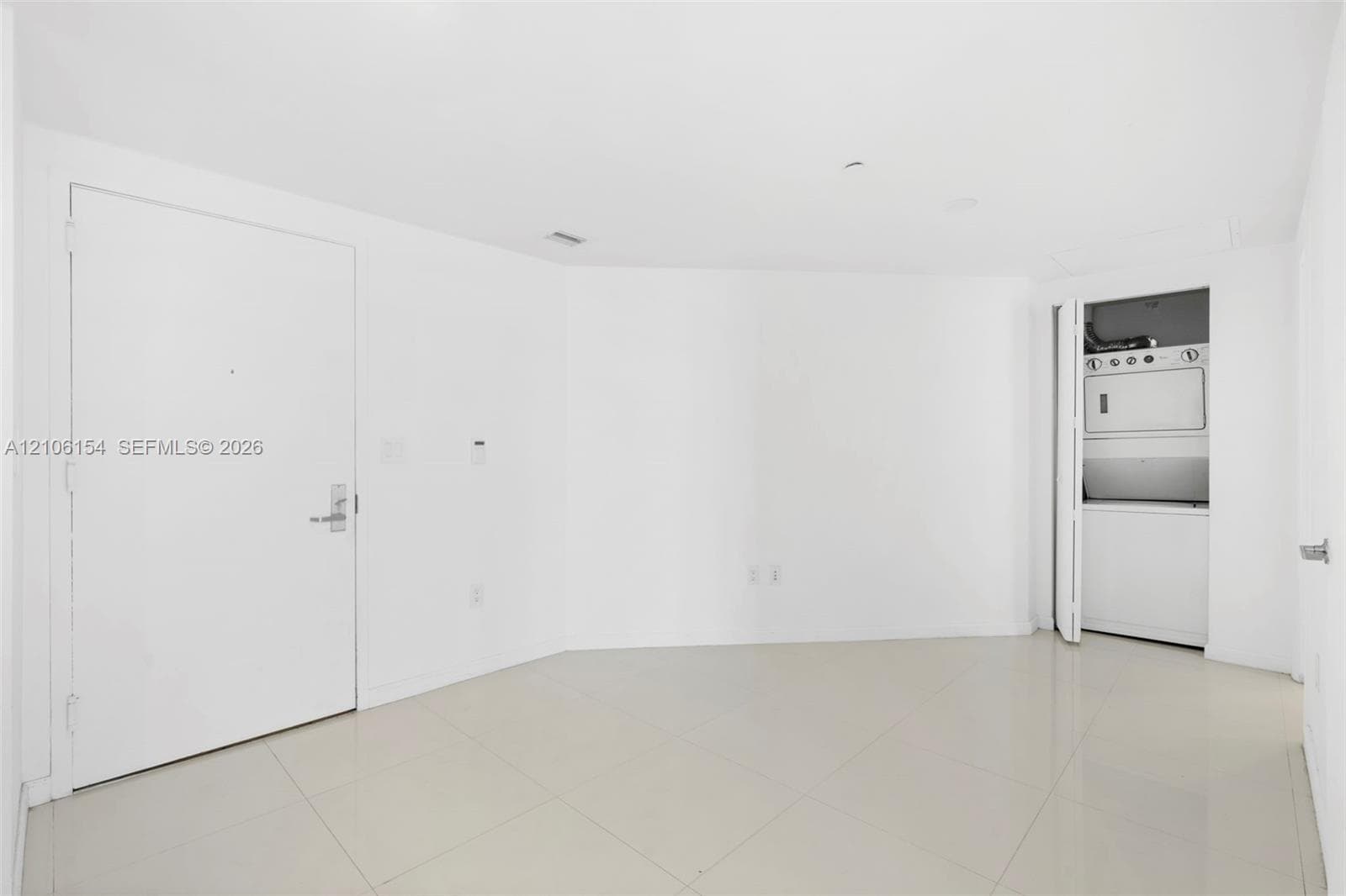 Interior area featuring neutral tile flooring, smooth white walls, and a recessed laundry closet equipped with a stacked washer and dryer unit
