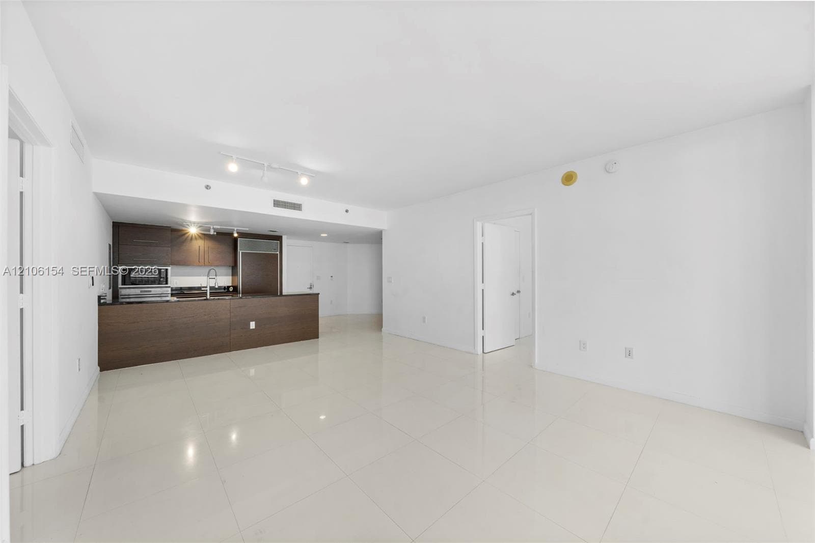 Open-concept kitchen featuring dark wood-finish cabinetry, built-in stainless steel appliances, dark countertops, and large-format tile flooring