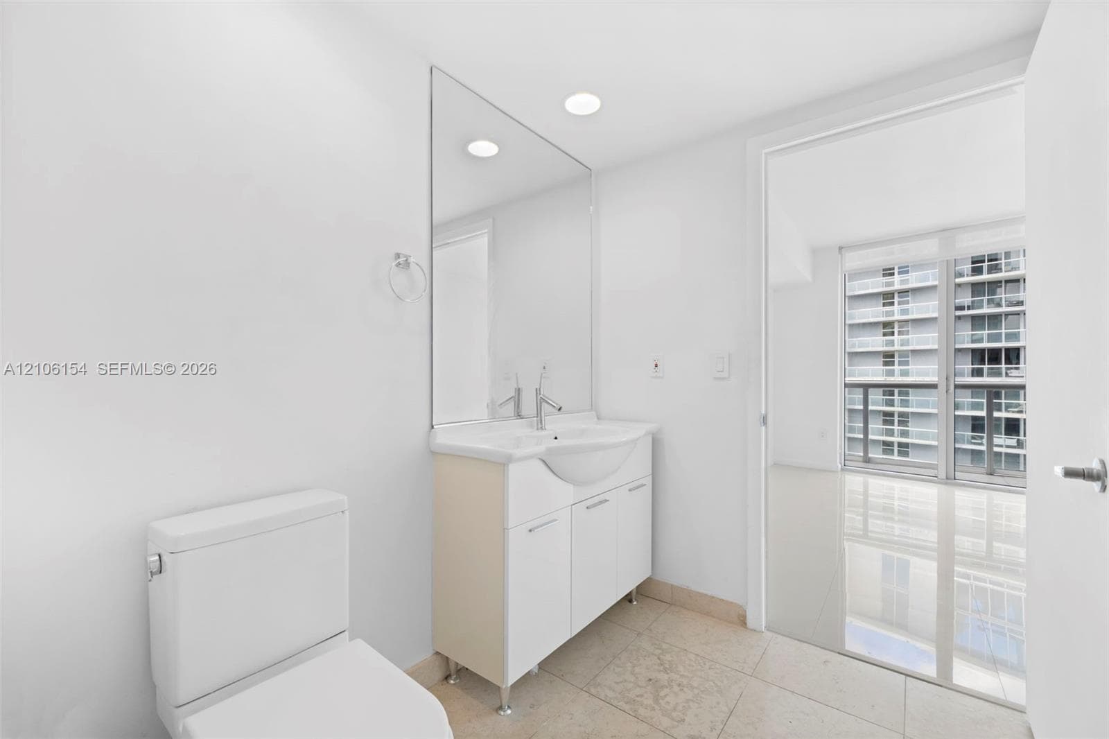 Bathroom featuring a white vanity cabinet, integrated sink, polished chrome faucet, large wall-mounted mirror, and tile flooring