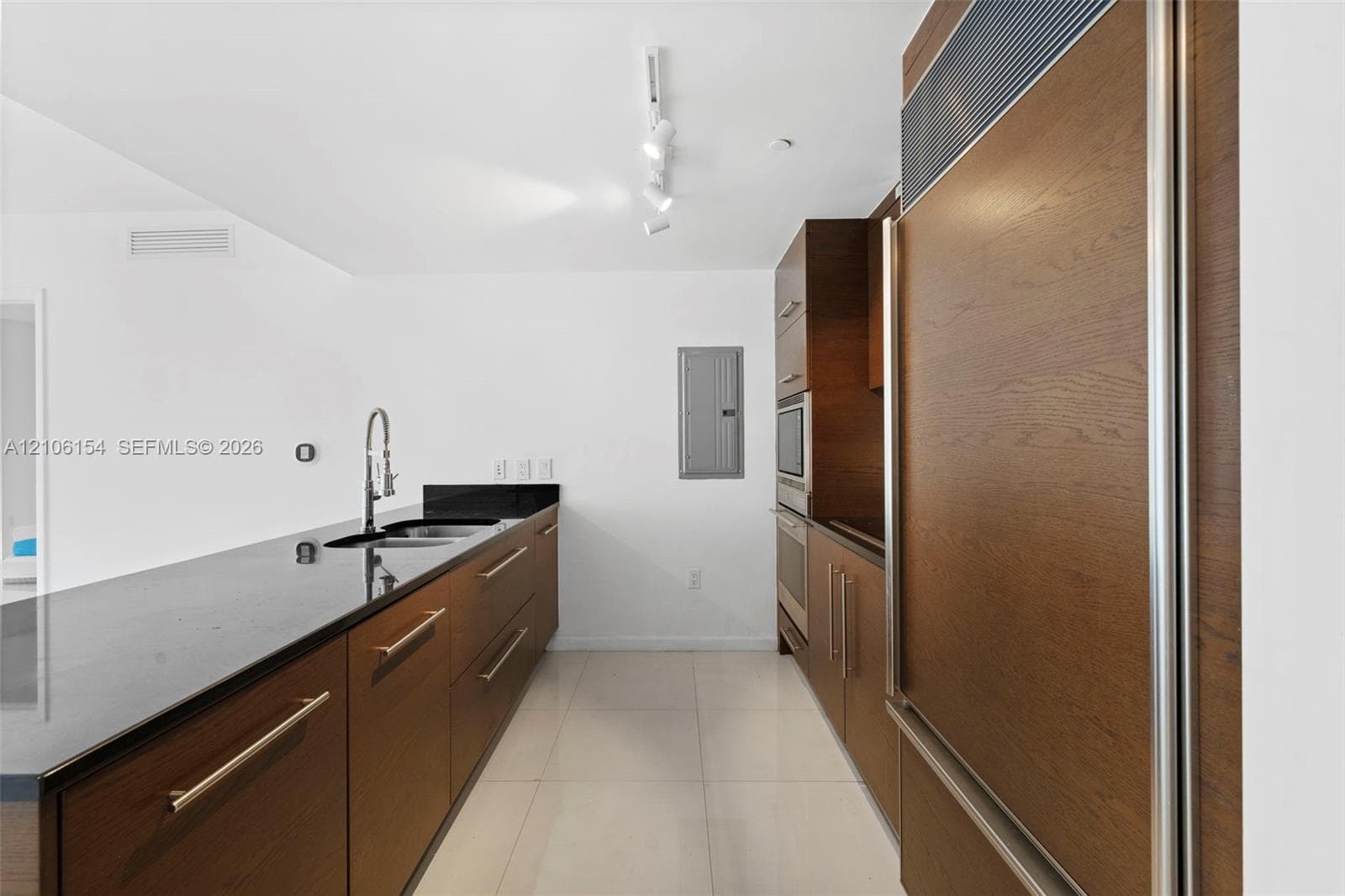 Custom cabinetry with wood-finish paneling, integrated refrigerator, sleek black countertops, stainless steel undermount sink with goose-neck faucet, and polished tile flooring