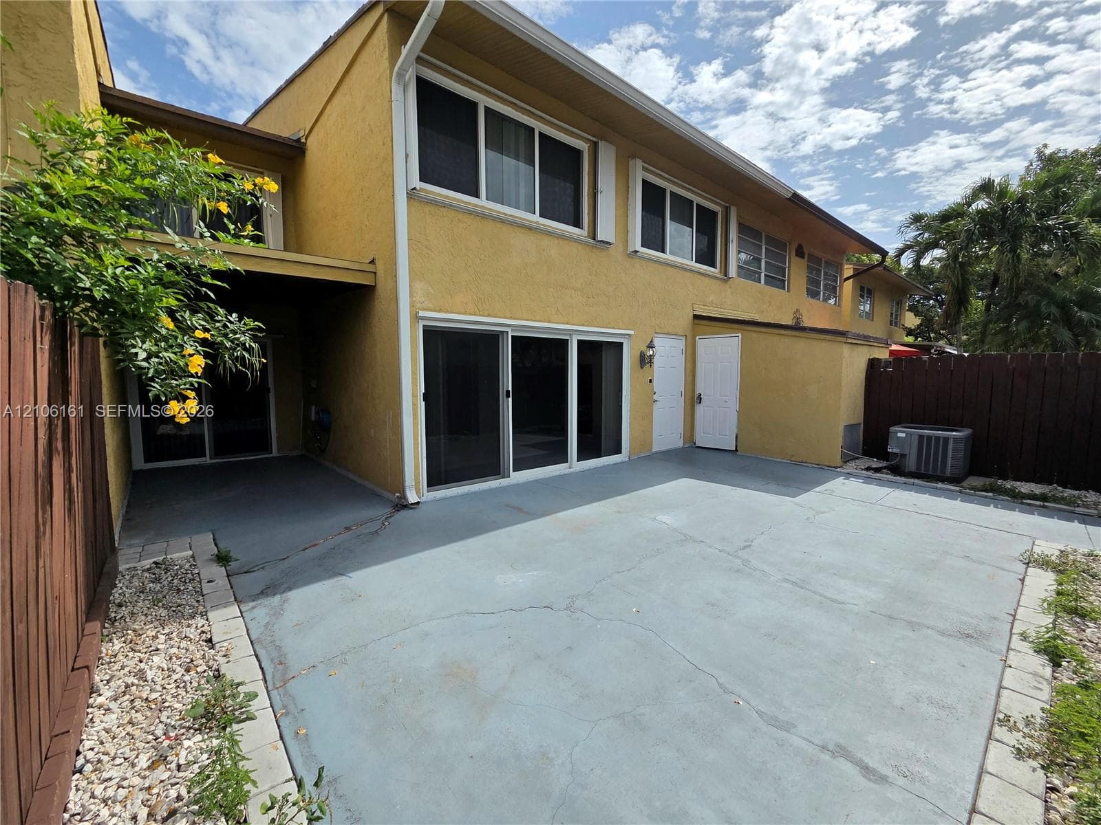 Two-story stucco exterior featuring a large concrete patio, sliding glass doors, and a wood privacy fence
