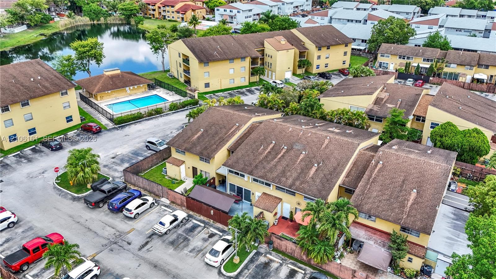 Aerial perspective featuring multi-story residential buildings, paved surface parking, and a community swimming pool