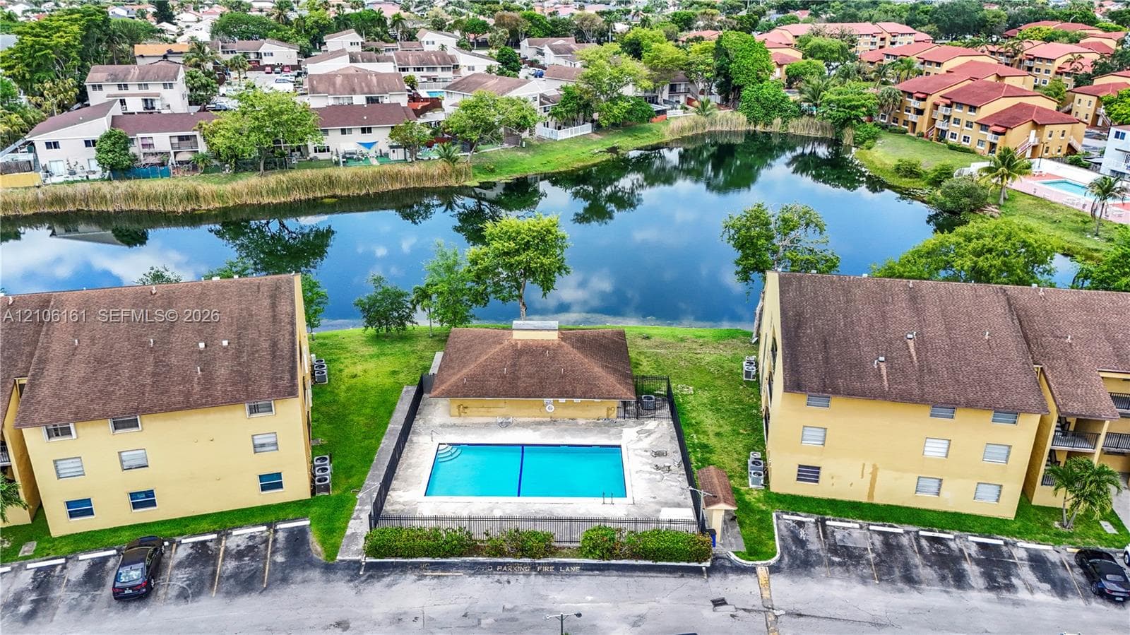 Aerial perspective featuring a swimming pool, surrounding concrete deck, black perimeter fencing, and water frontage