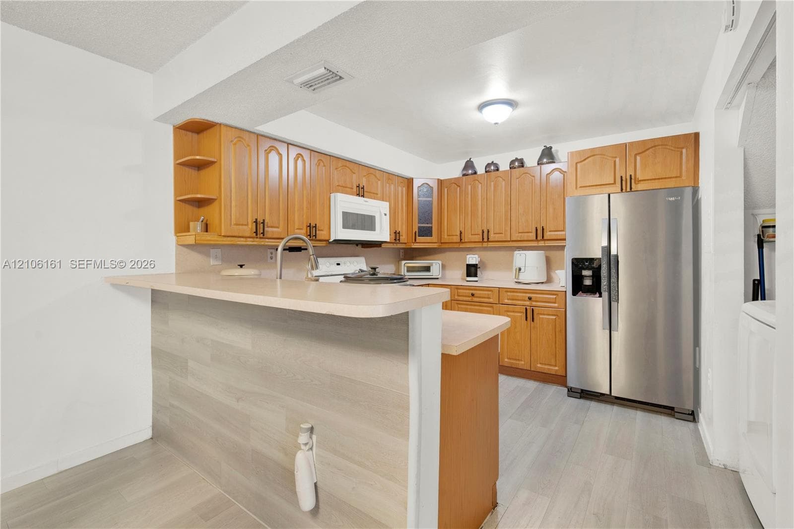 Kitchen featuring wood cabinetry, breakfast bar with wood-finish paneling, laminate countertops, stainless steel side-by-side refrigerator, and wood-finish flooring