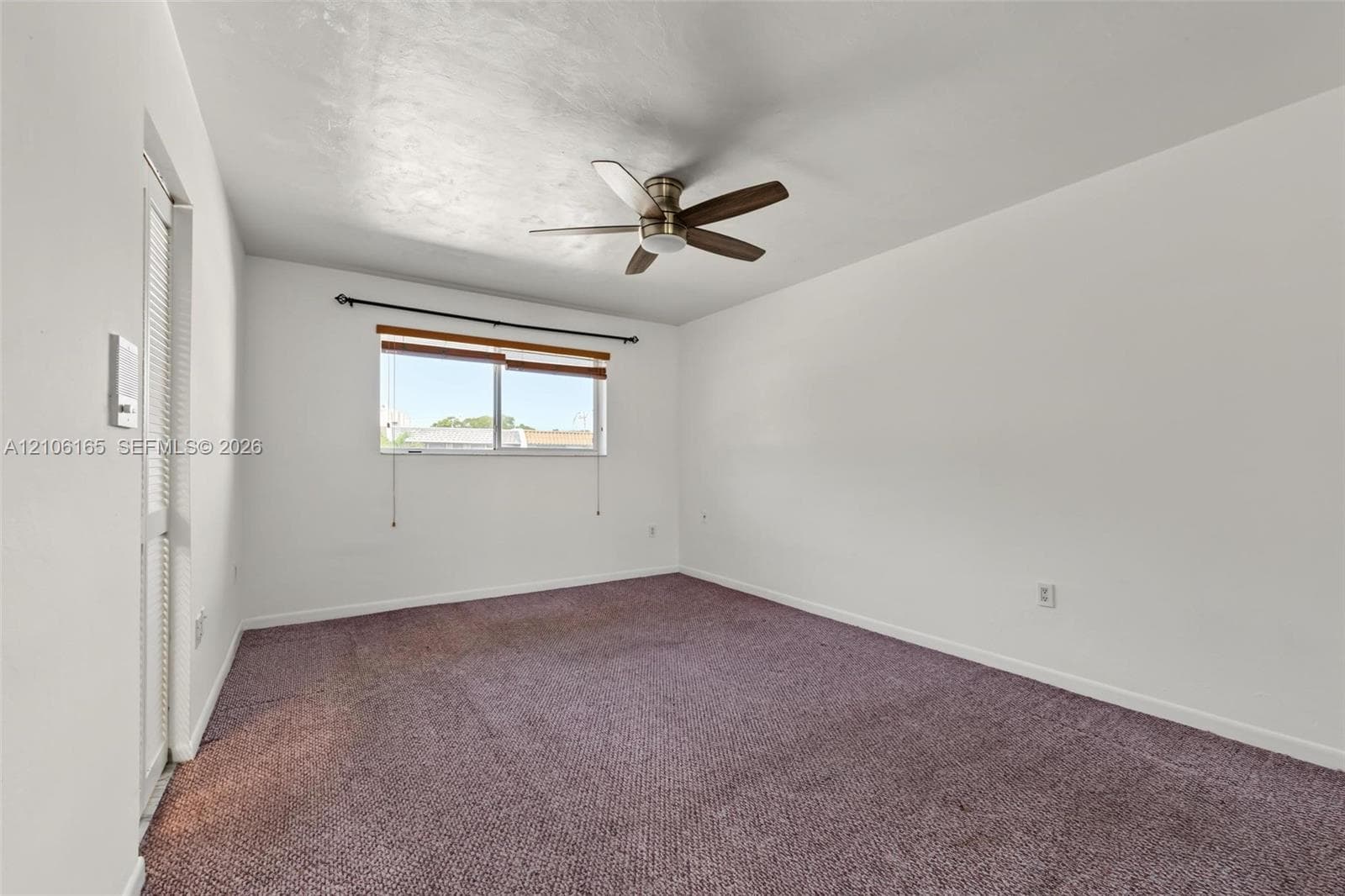 Interior room featuring wall-to-wall carpeting, a ceiling fan with integrated light fixture, a single-hung window with a dark metal curtain rod, and a louvered bi-fold closet door