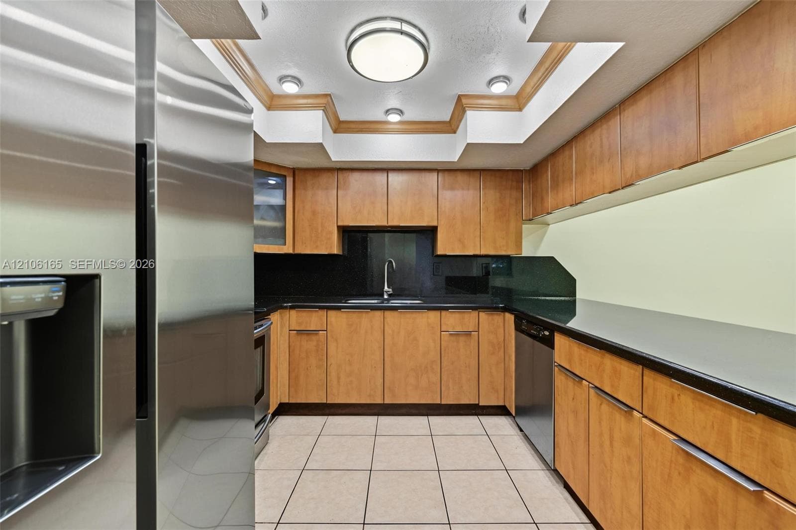 Kitchen featuring wood-finish cabinetry, solid surface countertops, stainless steel appliances, a tray ceiling with recessed lighting, and tile flooring