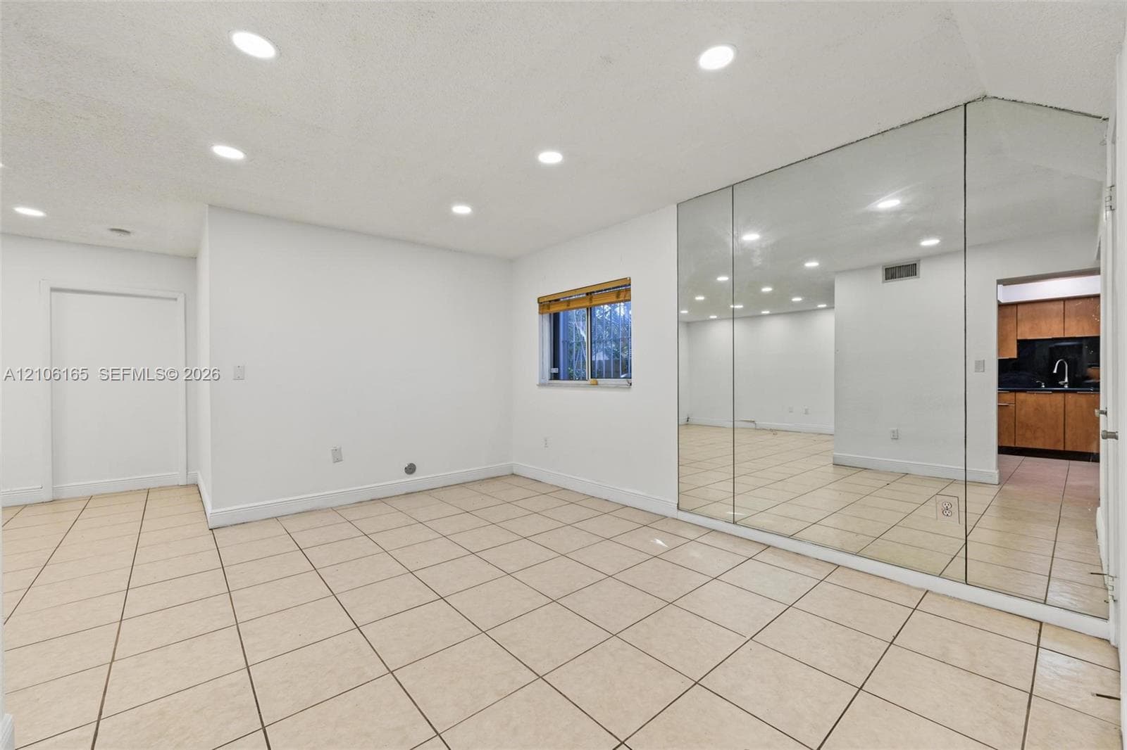 Interior space featuring neutral tile flooring, recessed ceiling lighting, a floor-to-ceiling mirrored wall, and a single window