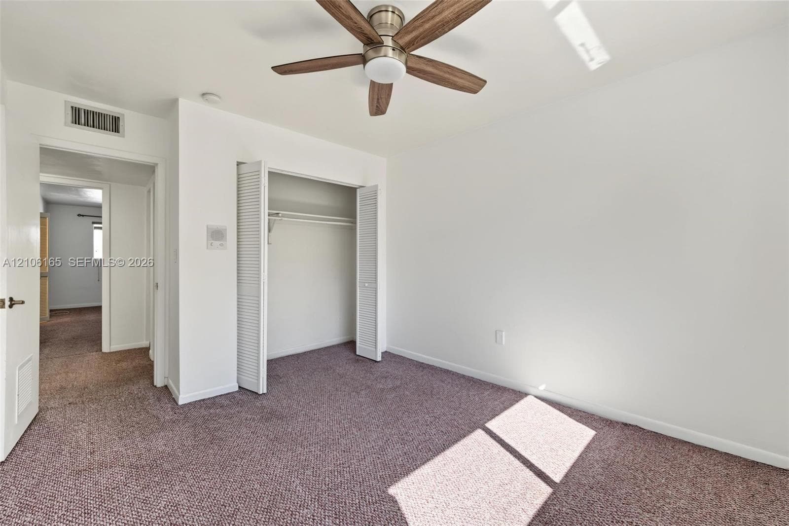 Interior room featuring wall-to-wall carpeting, a ceiling fan with integrated lighting, and a reach-in closet with louvered doors